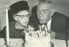 Mrs. Gertrude Miller and John Holmes blowing out candles at Gordon Head Mutual Improvement Society 70th anniversary